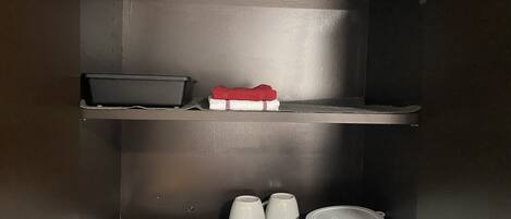 A dark-colored cabinet with shelves containing kitchenware, including plates, cups, and a red and white cloth.