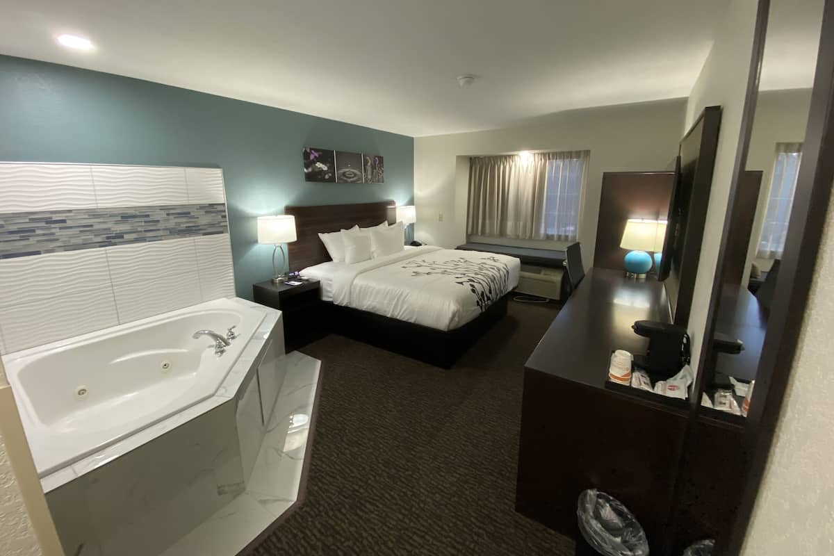 A hotel room with a large bed, a separate bathroom with a bathtub, a desk with a chair, and a large mirror.