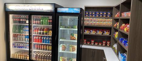 A vending machine area with a 'Cold Drinks' sign, a refrigerated display case, and shelves stocked with snacks and beverages.