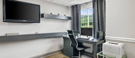 A modern office space with a flat-screen monitor, a desk, a chair, a printer, and a window with curtains.