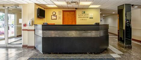 A hotel reception area with a reception desk, a clock, and a sign for 'Quality Inn & Suites'.