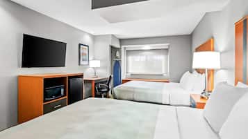 Une chambre d’hôtel avec deux lits, un téléviseur à écran plat, un bureau avec une chaise, un four à micro-ondes et une fenêtre avec des stores.