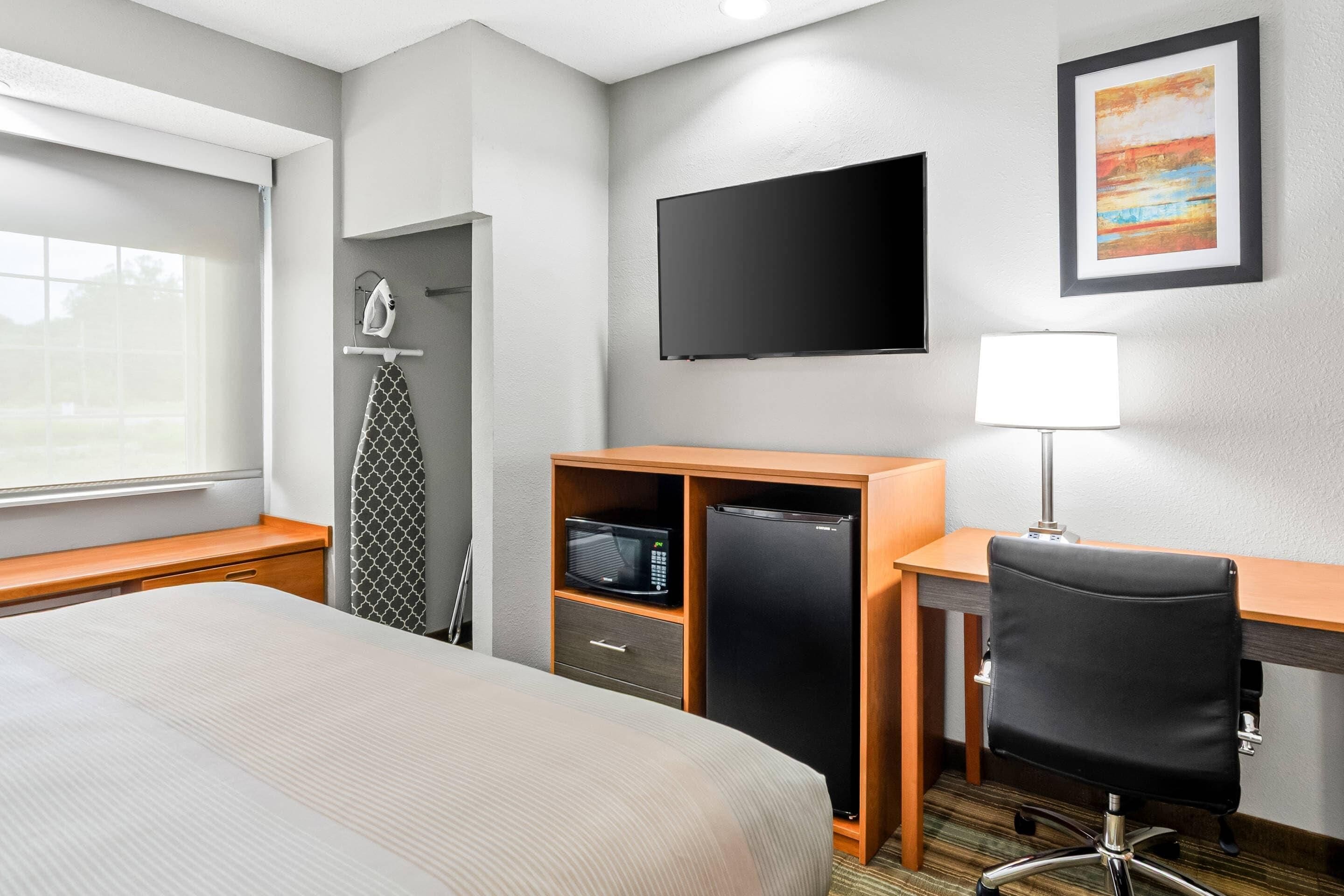Ein Hotelzimmer mit Bett, Schreibtisch mit Computer, Fernseher, Mikrowelle, Kühlschrank und einem Sessel.