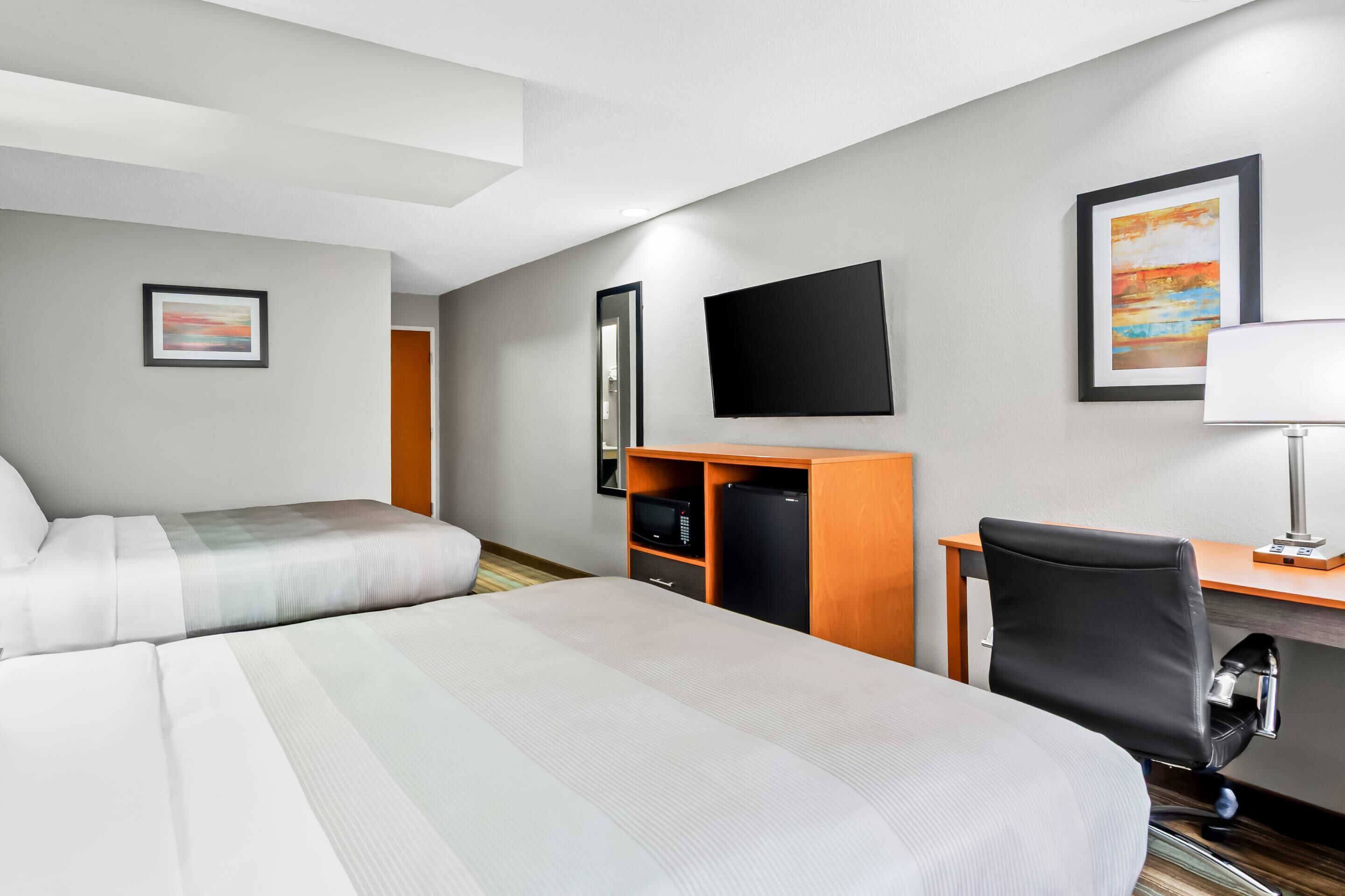 A hotel room with two beds, a desk, a chair, a TV, and a mirror.