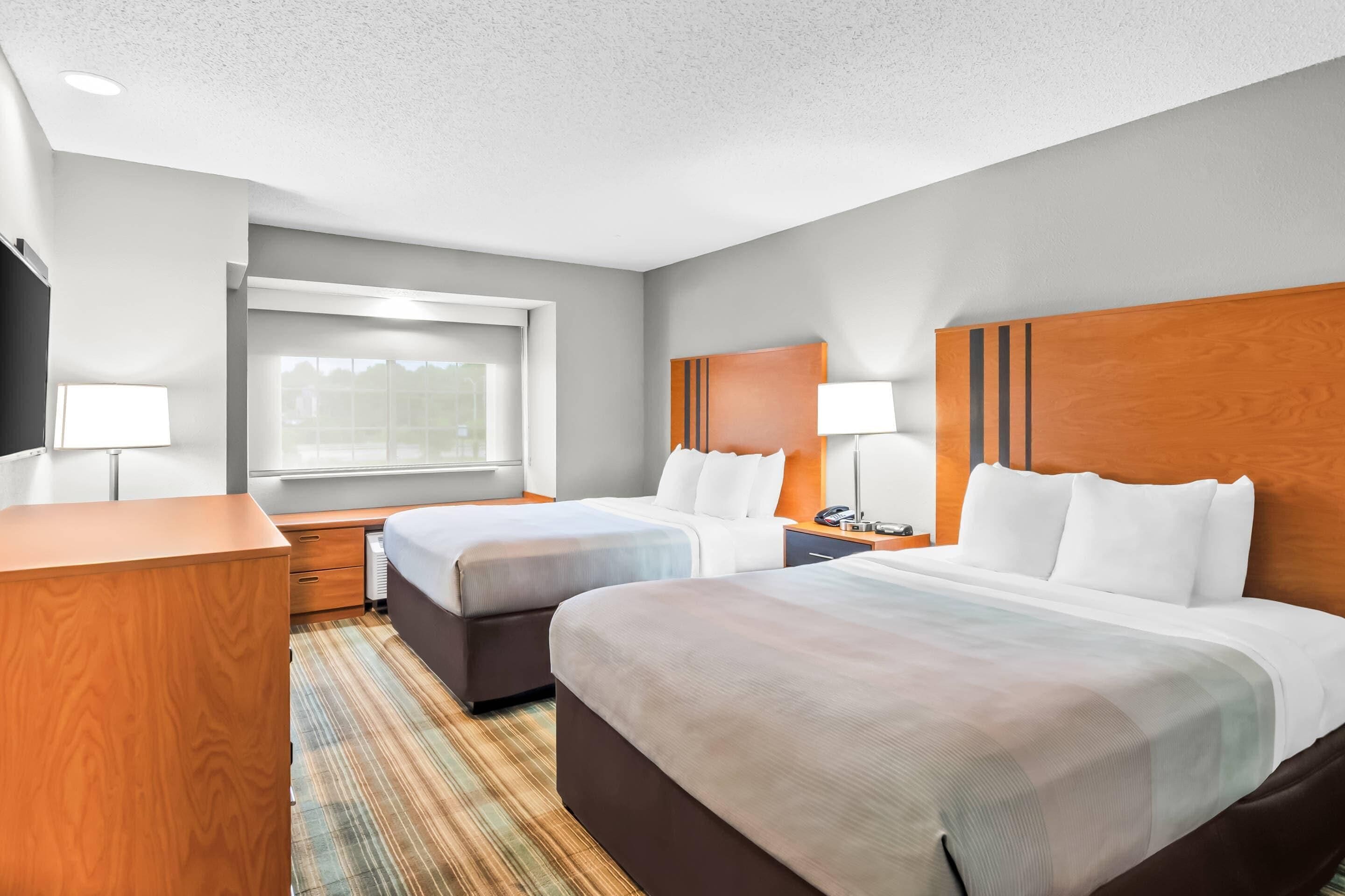 A hotel room with two beds, a desk, a window, and a view of the outdoors.