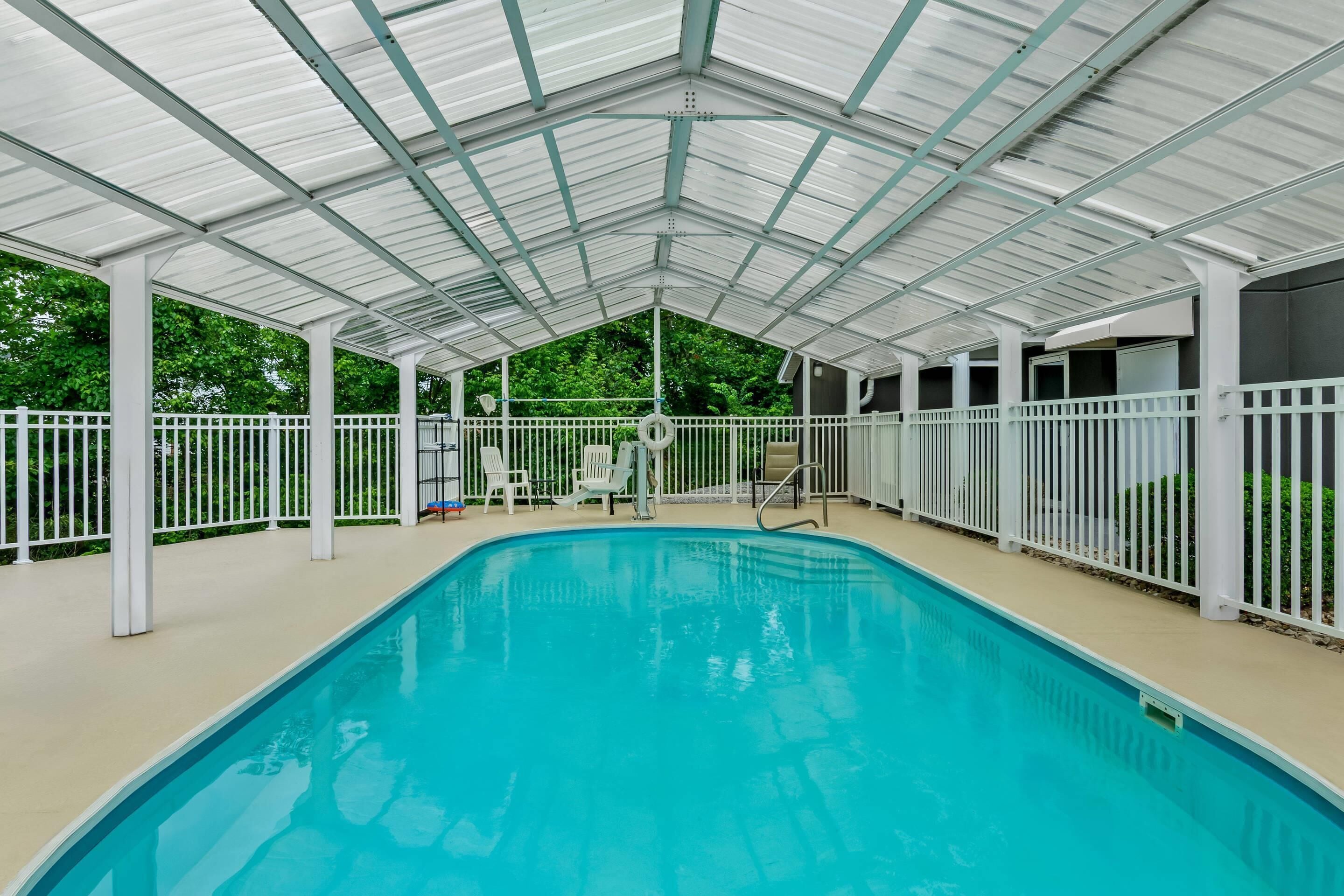 An indoor swimming pool with a covered roof, white railings, and a few lounge chairs.