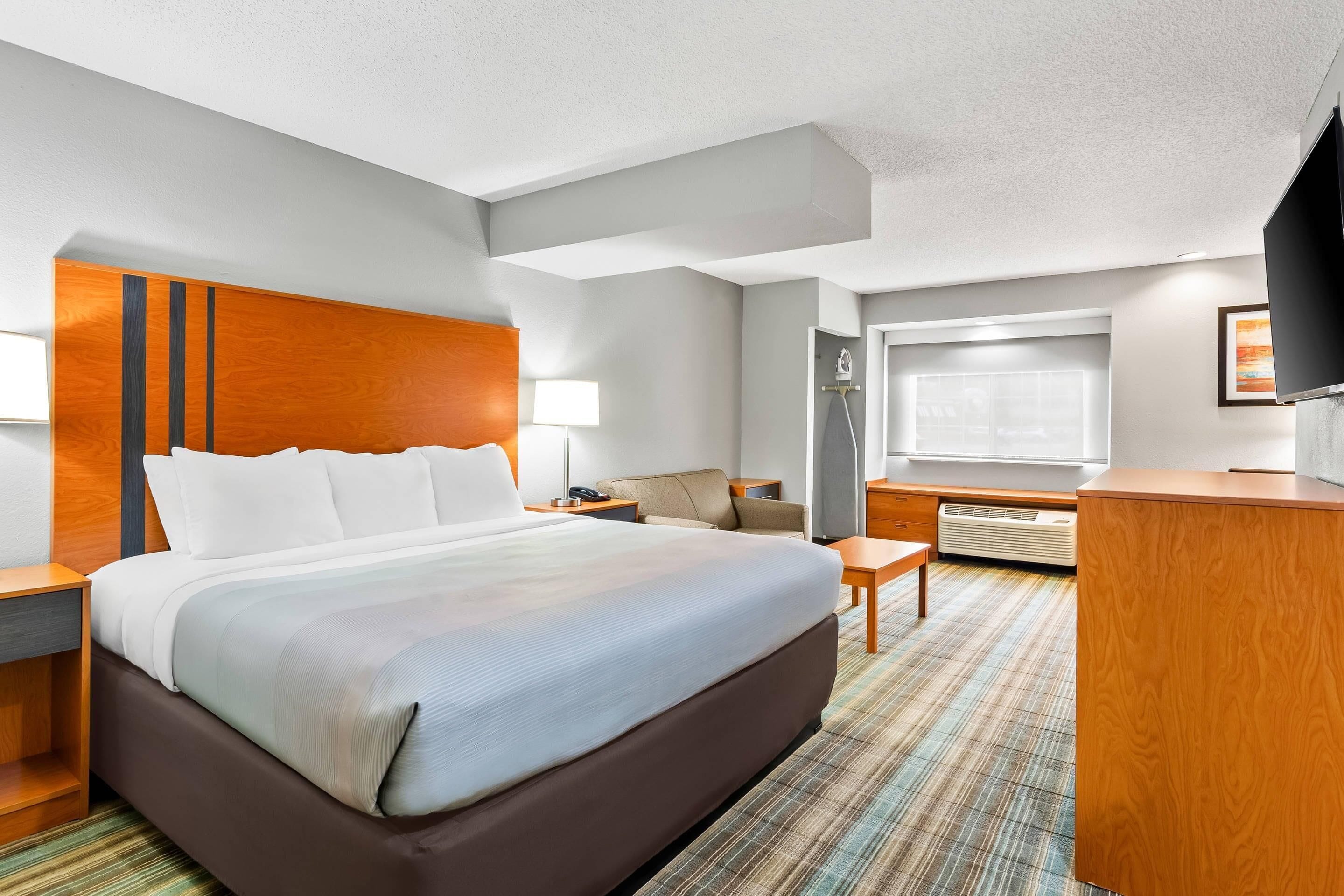 A hotel room with a large bed, a desk, a chair, a TV, and a window.