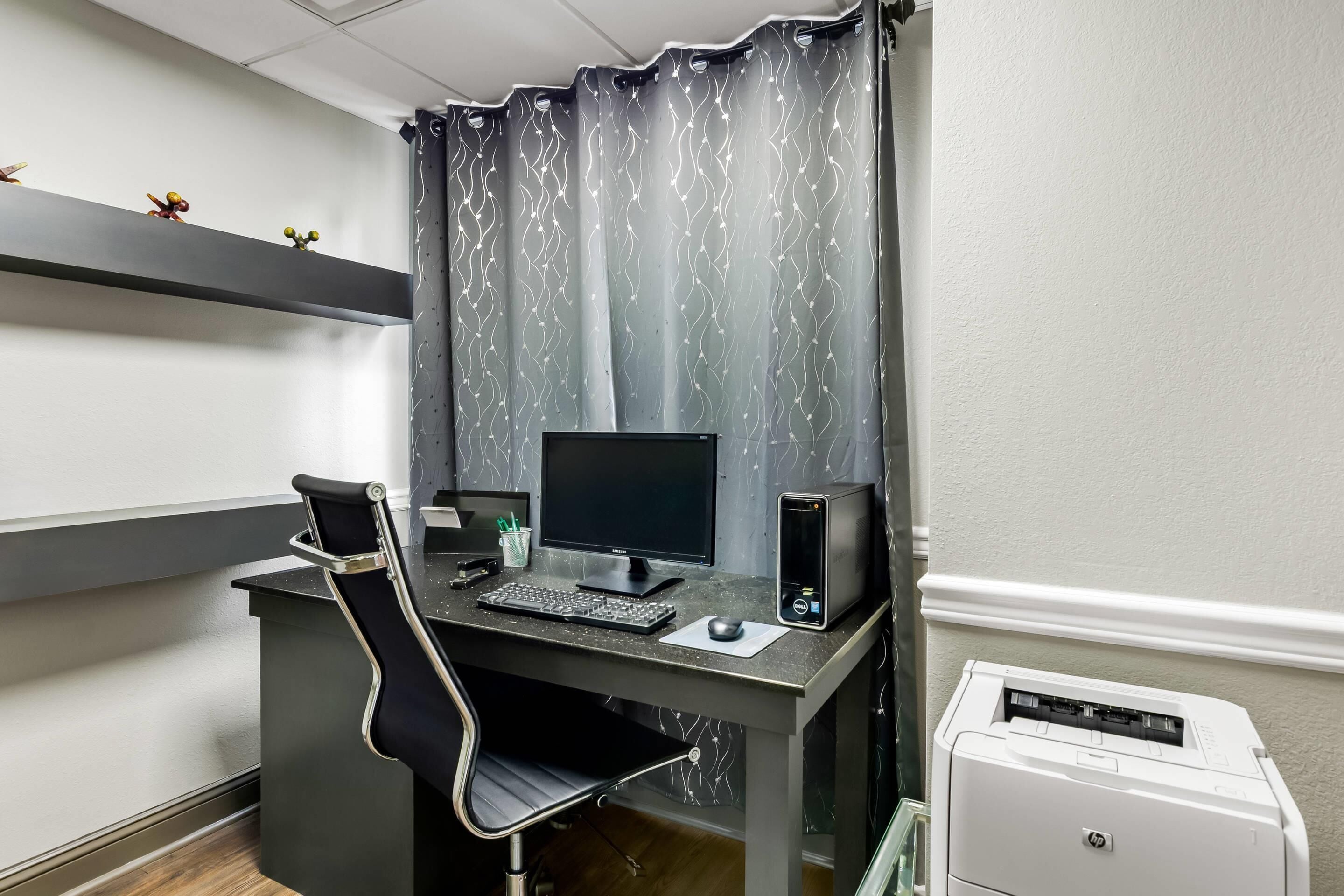 A home office setup with a desk, computer, chair, and printer.
