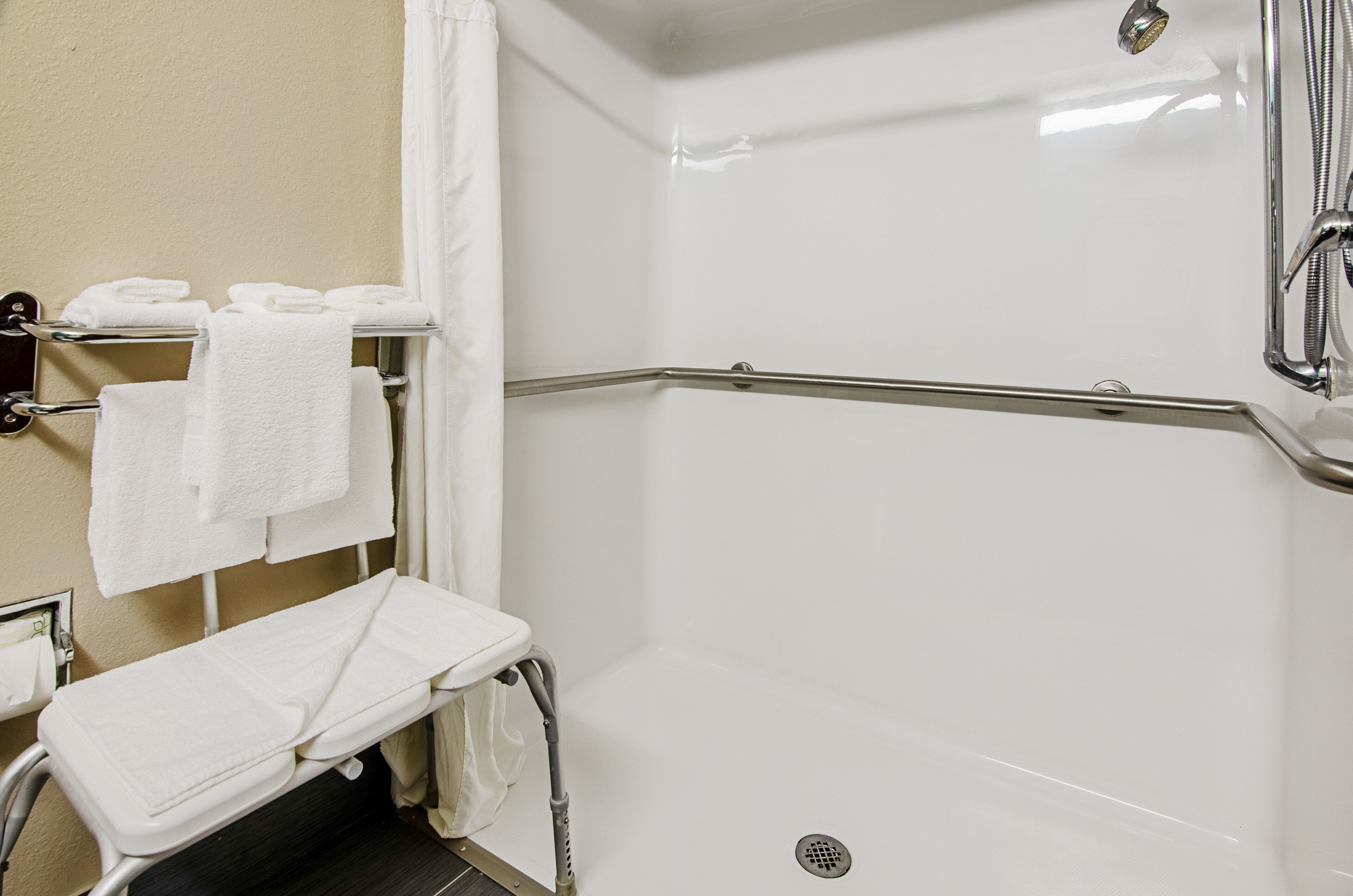 A white, modern bathroom with a shower, a bench, and a towel rack.