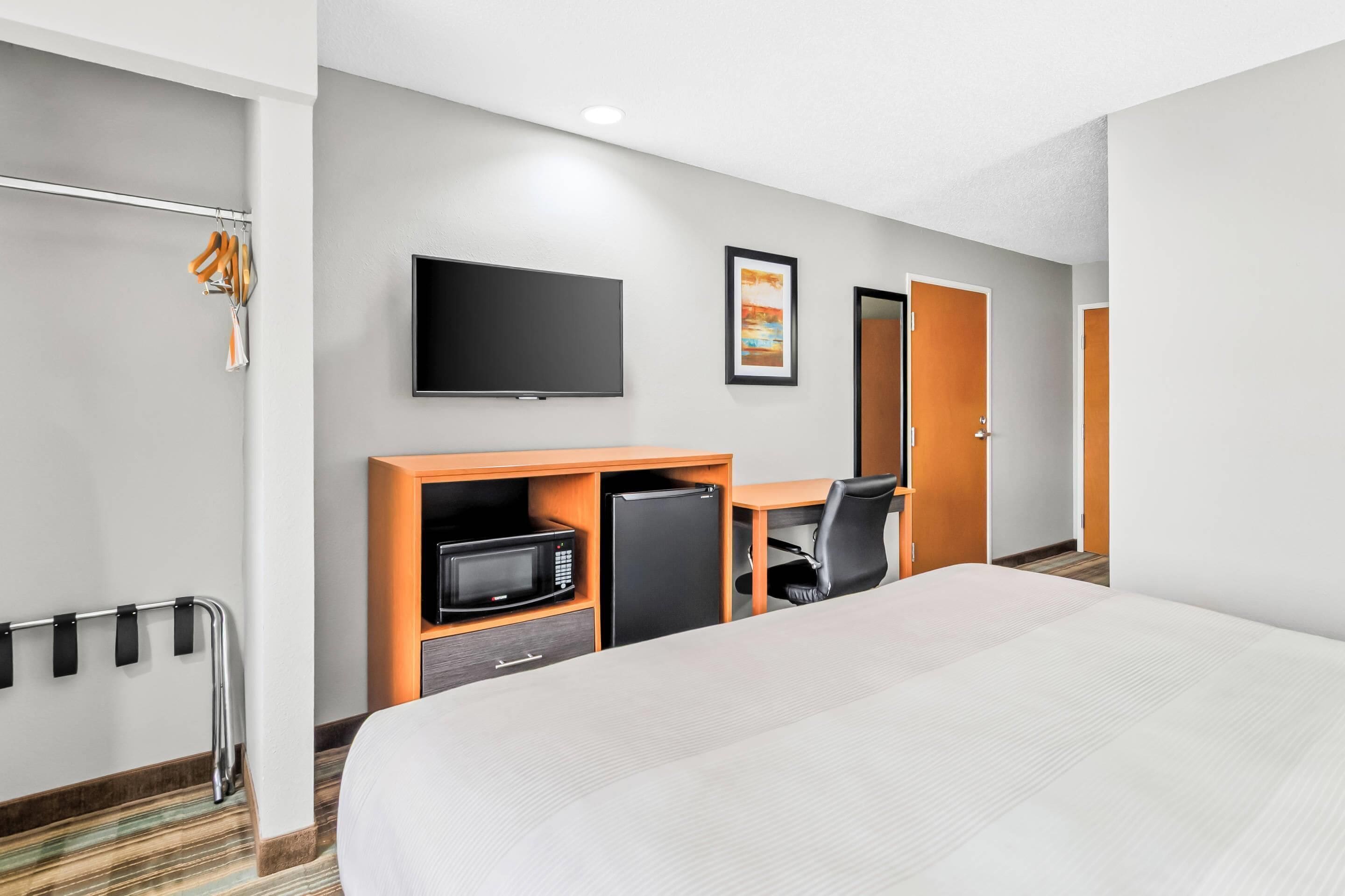 A hotel room with a bed, a desk with a chair, a television, a microwave, and a refrigerator.