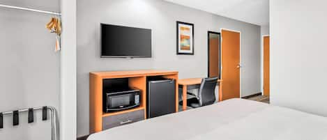 Habitación de hotel con cama, escritorio con silla, televisor, microondas y refrigerador.
