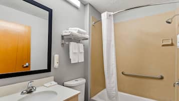 A bathroom with a sink, toilet, and shower. There are towels on a rack and a handrail in the shower.