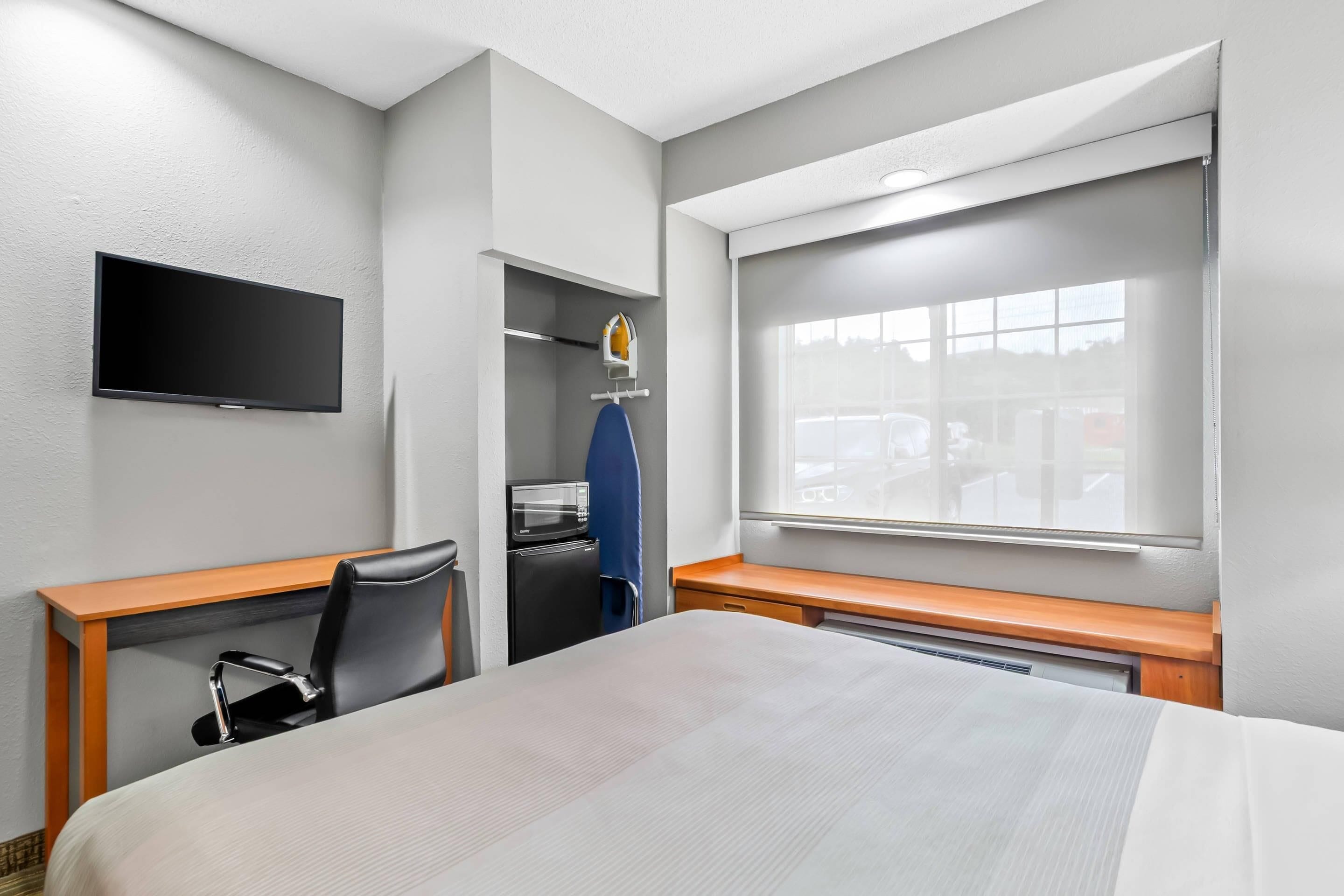 Camera d'albergo con un letto, una scrivania, una sedia, una TV a schermo piatto, un forno a microonde e una finestra con tende.