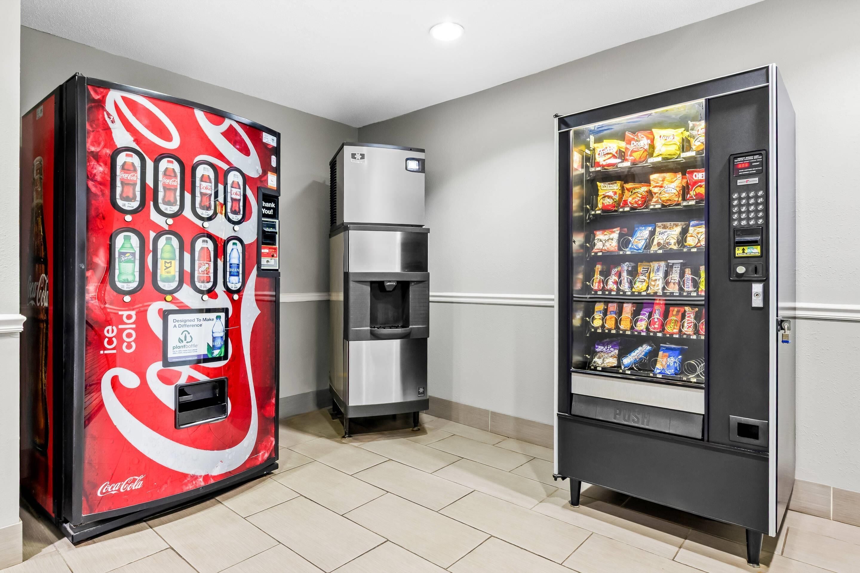 Two vending machines, one with Coca-Cola branding and another with snacks, in a hallway with tiled flooring.