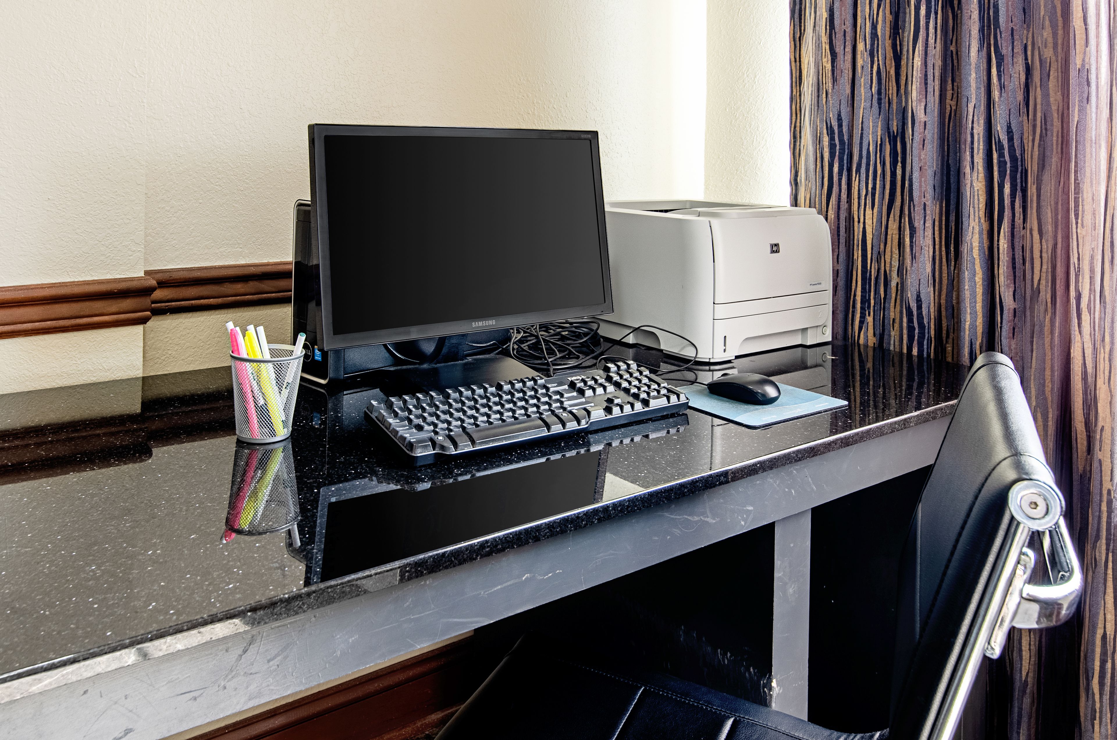 Un mostrador de hotel con una computadora de escritorio, una impresora, un teclado, un ratón y una silla.