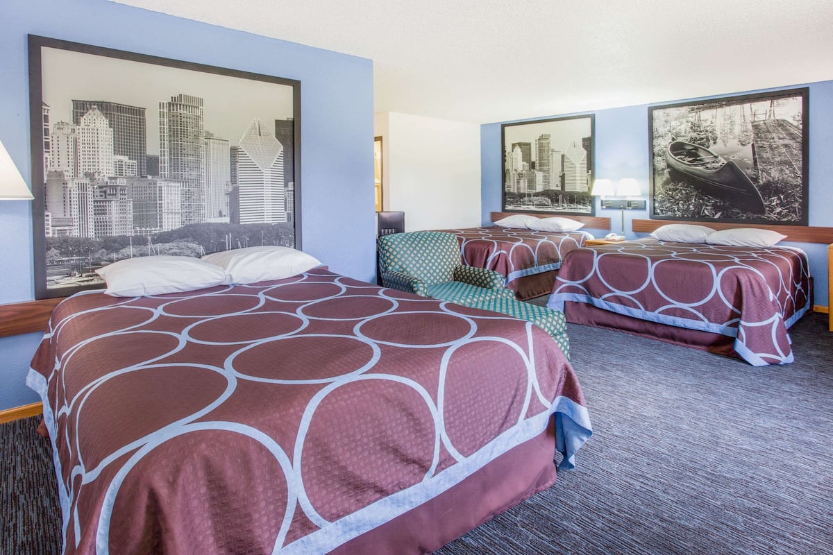 A hotel room with two beds, each with a patterned bedspread, a cityscape mural on the wall, and a framed picture of a boat.