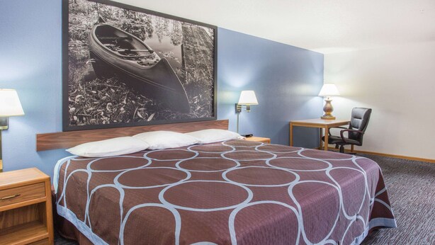 A hotel room with a large bed, a nightstand, a chair, a desk, and a wall-mounted lamp. - Super 8 by Wyndham Monmouth IL (Monmouth)