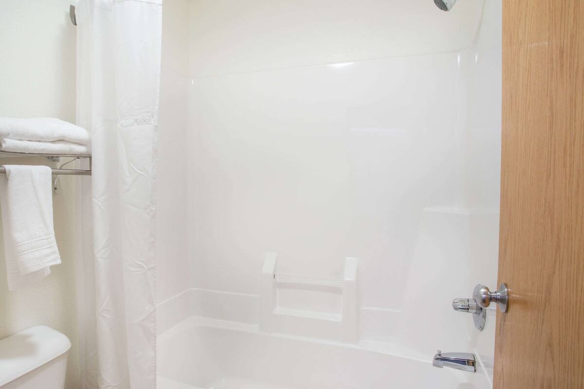 A bathroom with a white bathtub, a shower curtain, a towel rack with towels, and a wooden door.