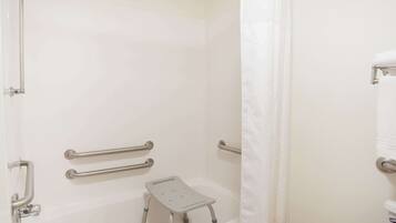 A bathroom with a bathtub, grab bars, a showerhead, and a white towel rack.