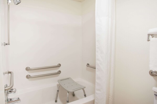 Un baño con bañera, barras de apoyo, cabezal de ducha y un perchero blanco.