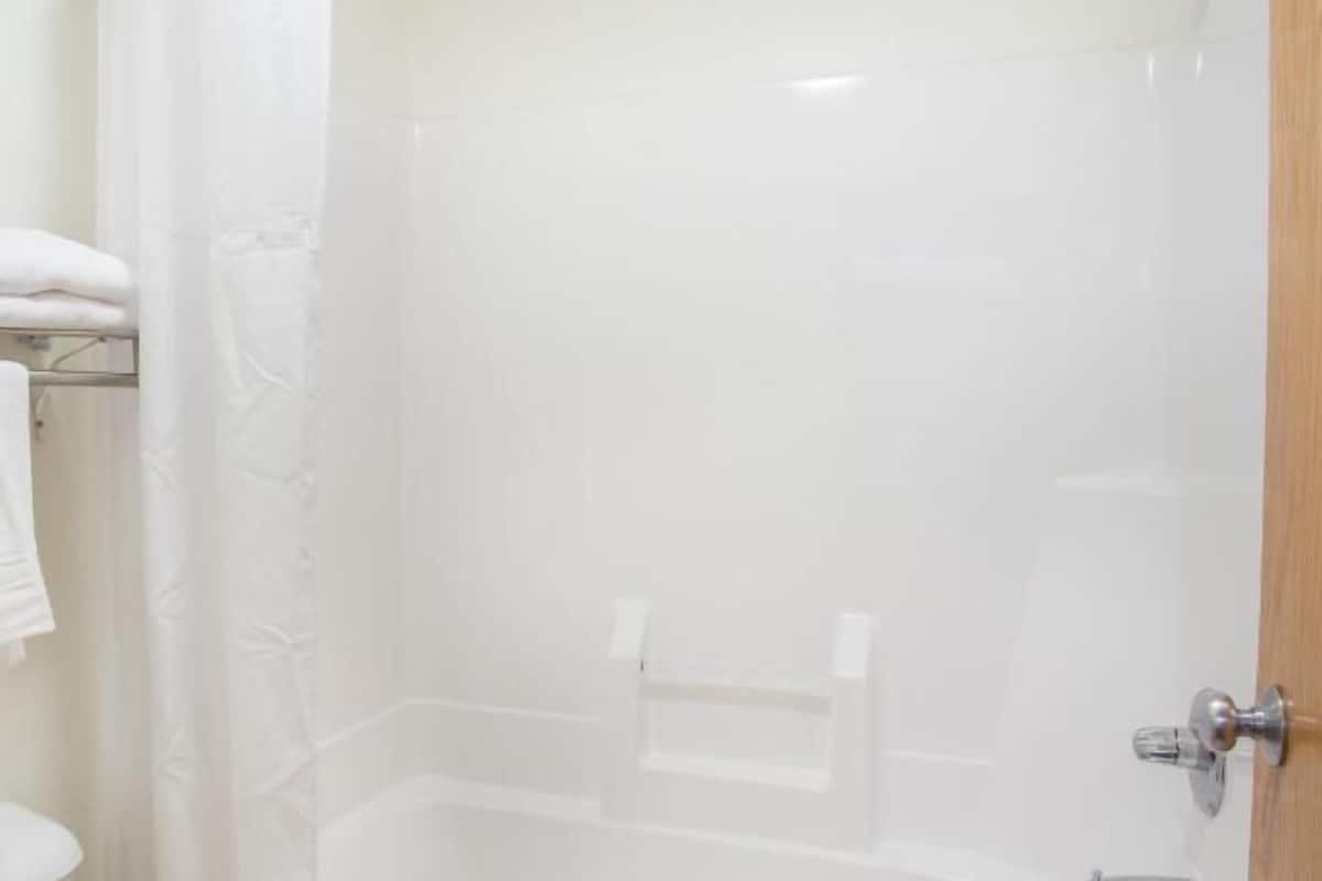 A bathroom with a shower, a towel rack, and a wooden door.