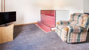 A room with a television on a wooden stand, a red and white tiled shower area, and a plaid-patterned armchair. - Super 8 by Wyndham Monmouth IL (Monmouth)