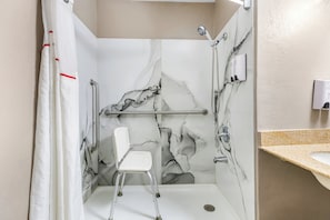 A shower stall with a marble wall, a white chair, and a handrail.