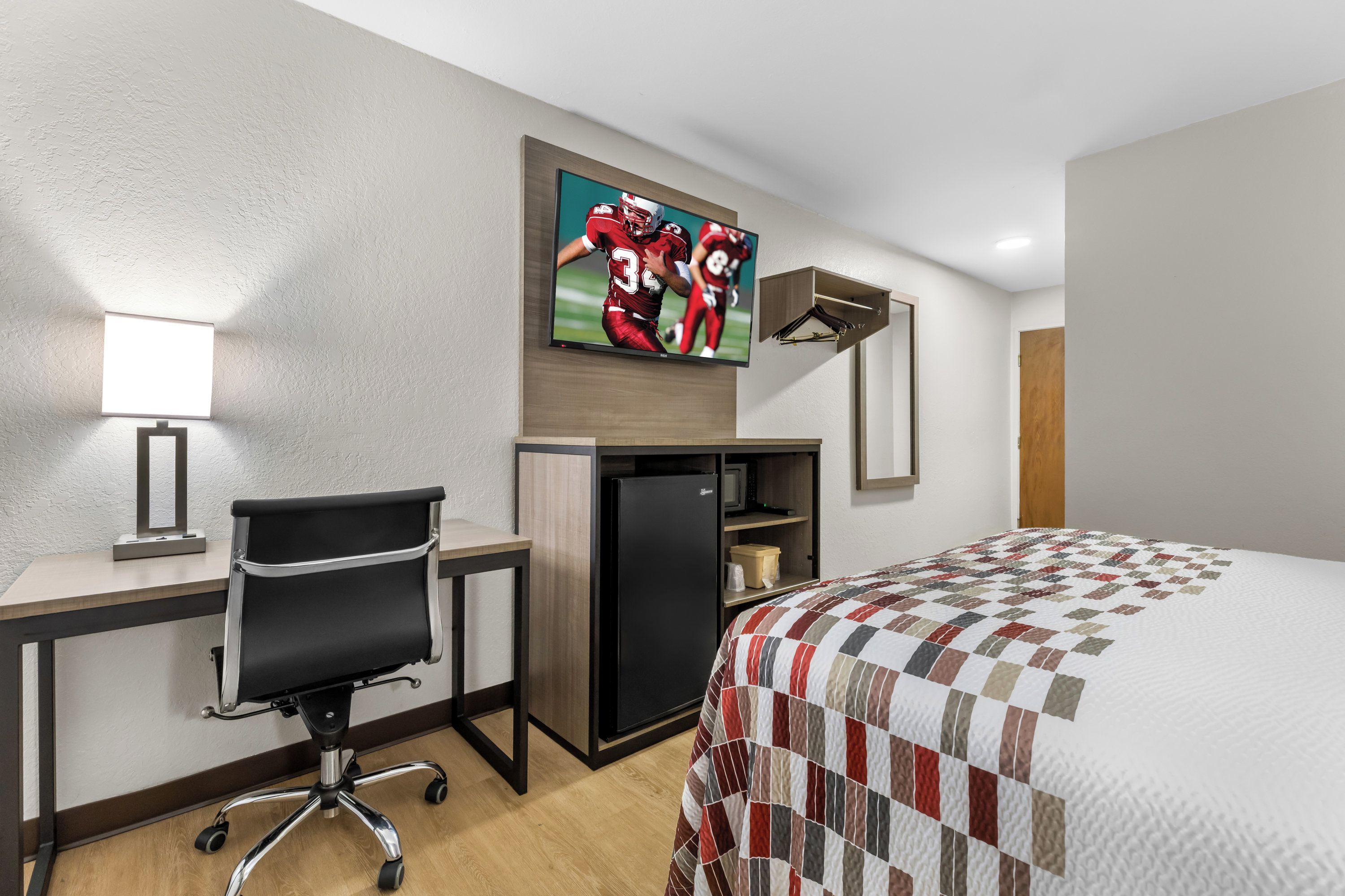 Een hotelkamer met een bed, bureau, stoel, televisie en een kleine koelkast.