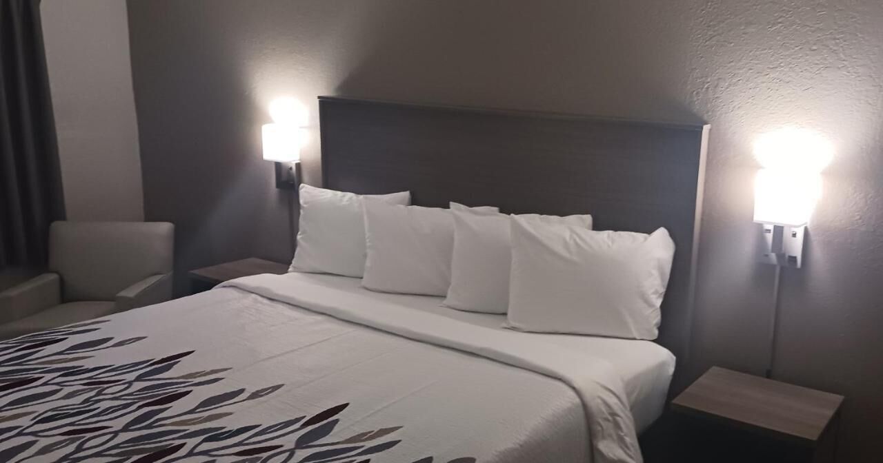 A hotel room with a bed, two bedside tables, a chair, and a wall-mounted lamp.