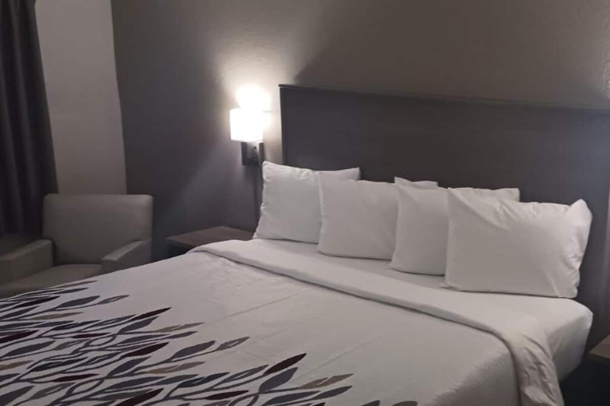 A hotel room with a bed, two bedside tables, a chair, and a wall-mounted lamp.