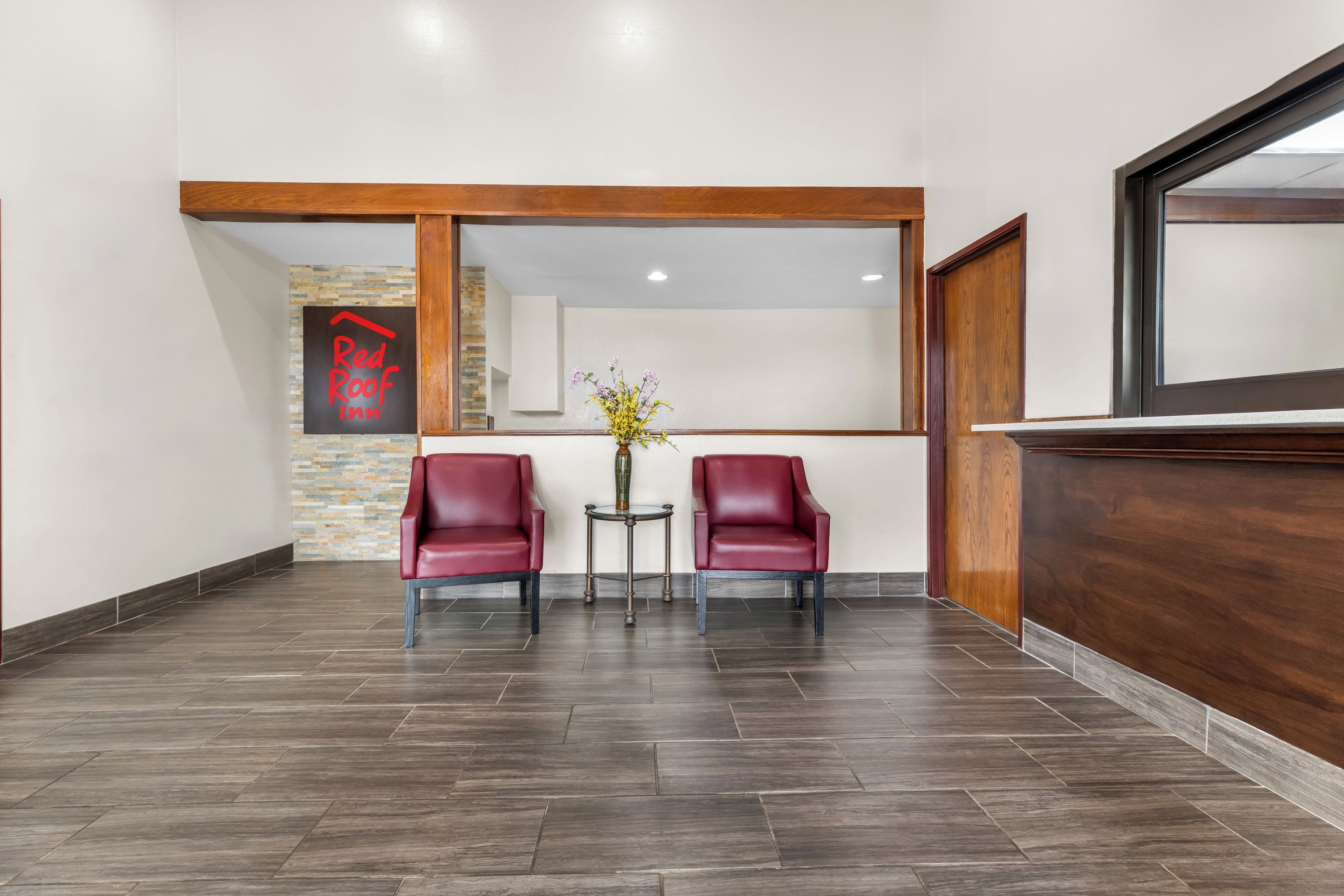 A reception area with two red leather chairs, a small table with a vase of flowers, and a wooden reception desk.