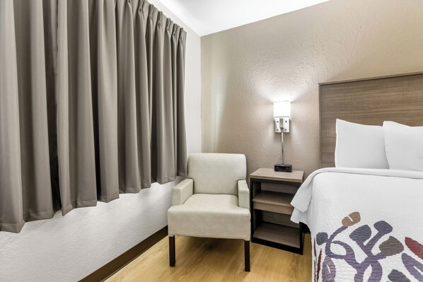 A hotel room with a bed, a chair, a desk, and a lamp.