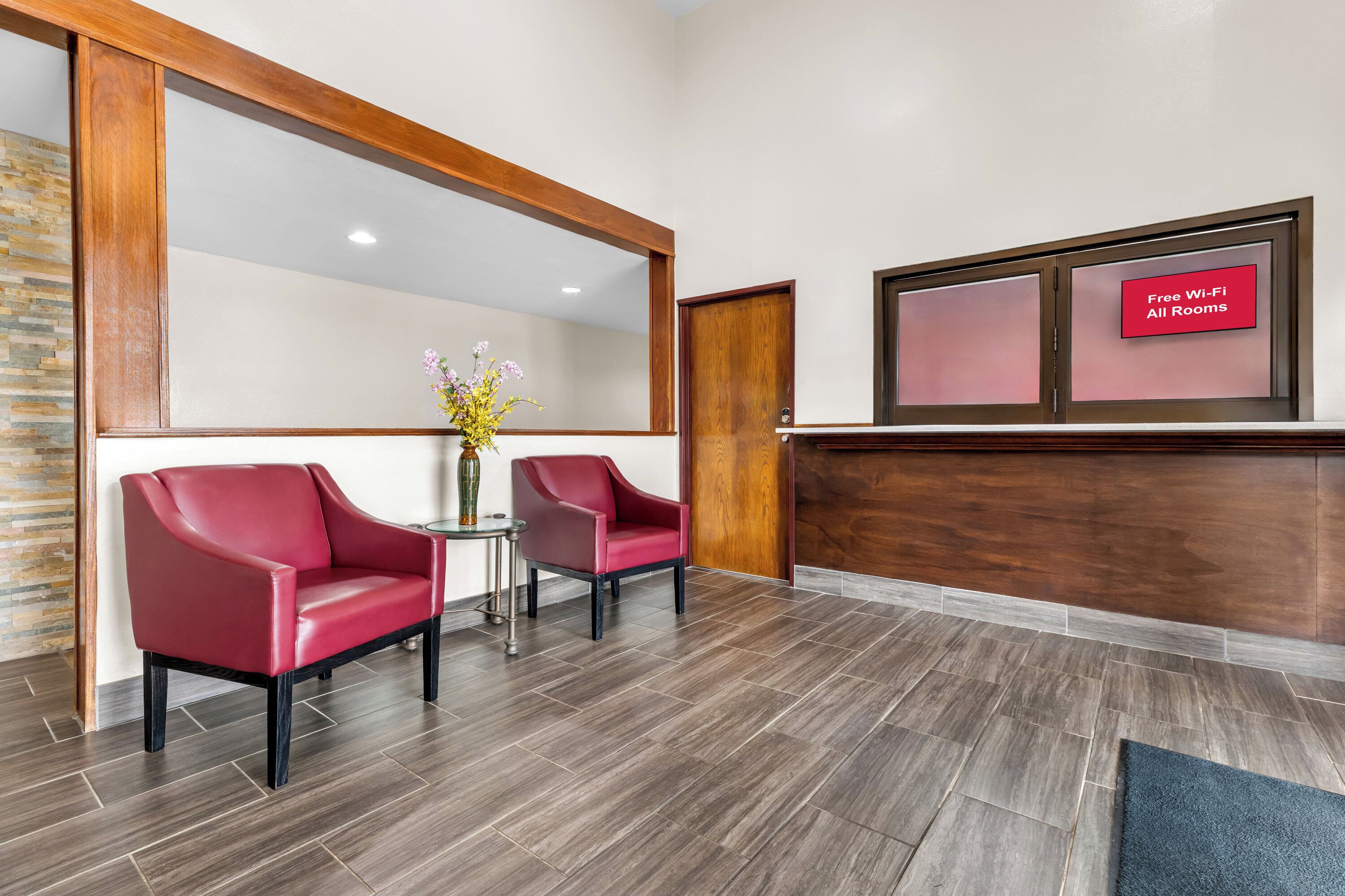 A reception area with two red leather chairs, a small table with a vase, and a sign indicating free Wi-Fi in all rooms.