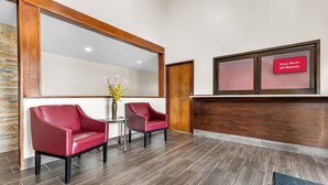 Un área de recepción con dos sillones de cuero rojo, una mesita con un florero, y un cartel que indica Wi-Fi gratuito en todas las habitaciones.