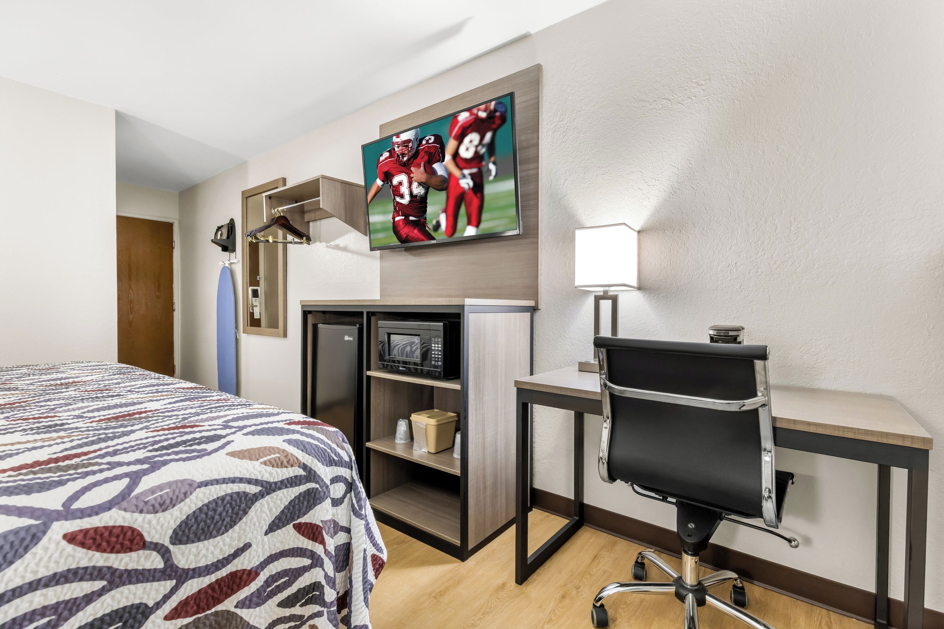 Une chambre d’hôtel équipée d’un lit, d’un bureau, d’une chaise, d’une télévision, d’un four à micro-ondes et d’une étagère.