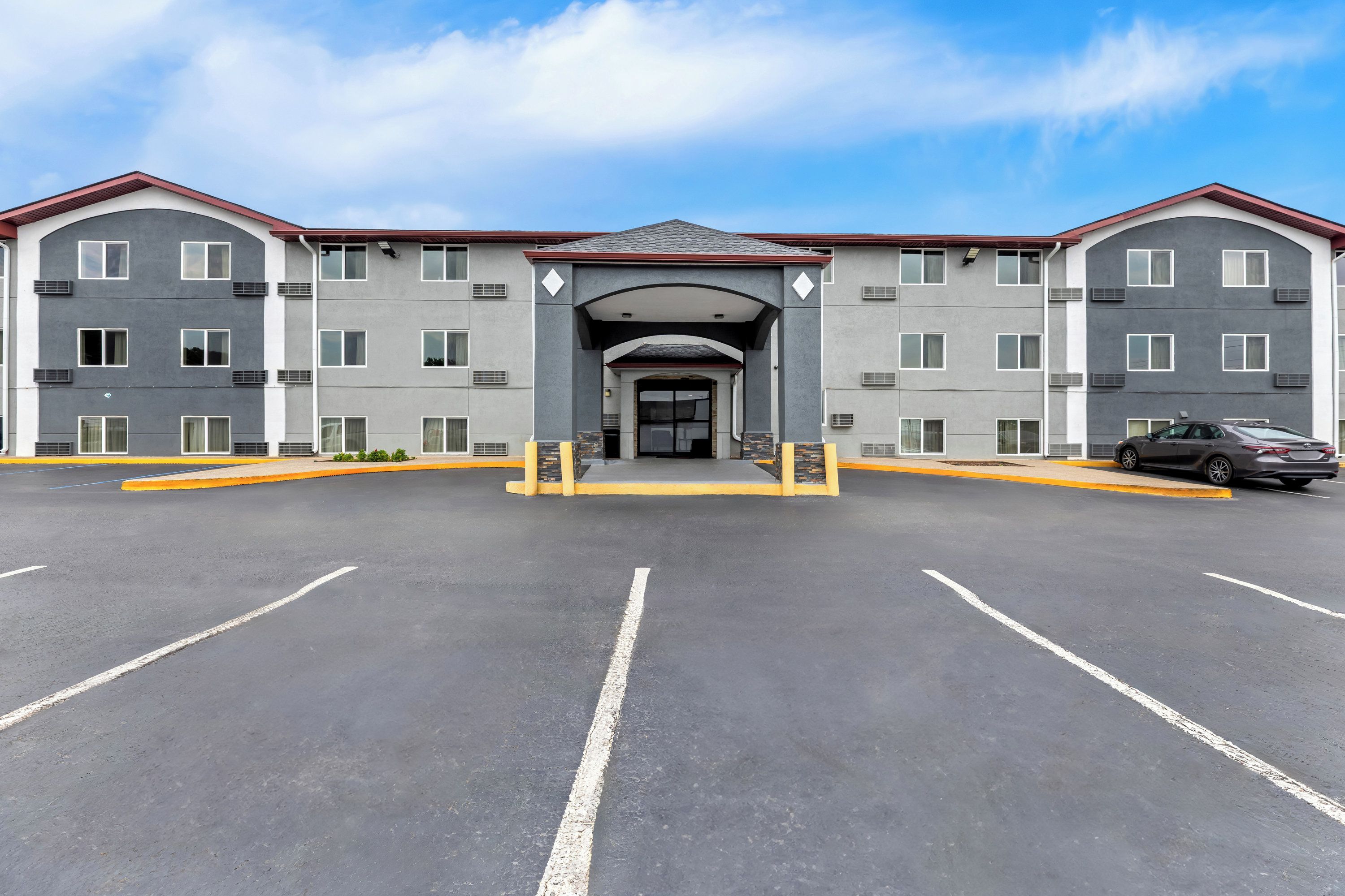 A multi-story hotel with a central entrance, a parking lot, and a car parked in the lot.