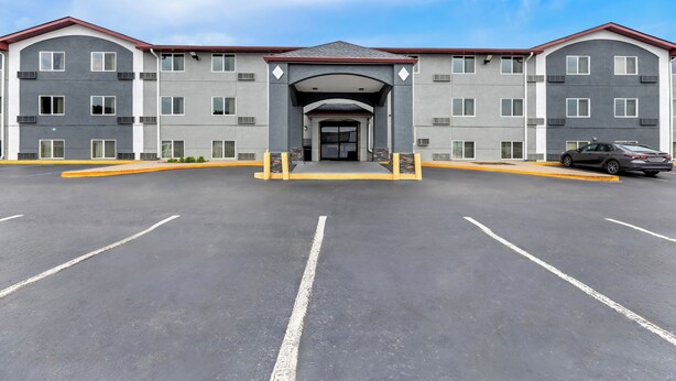 Un hotel de varios pisos con una entrada central, un estacionamiento y un coche dentro.