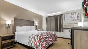 A hotel room with a bed, bedside tables, a desk, a TV, and a window with curtains.