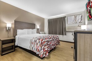 A hotel room with a bed, bedside tables, a desk, a TV, and a window with curtains. - Red Roof Inn Huntsville, AL (Huntsville)