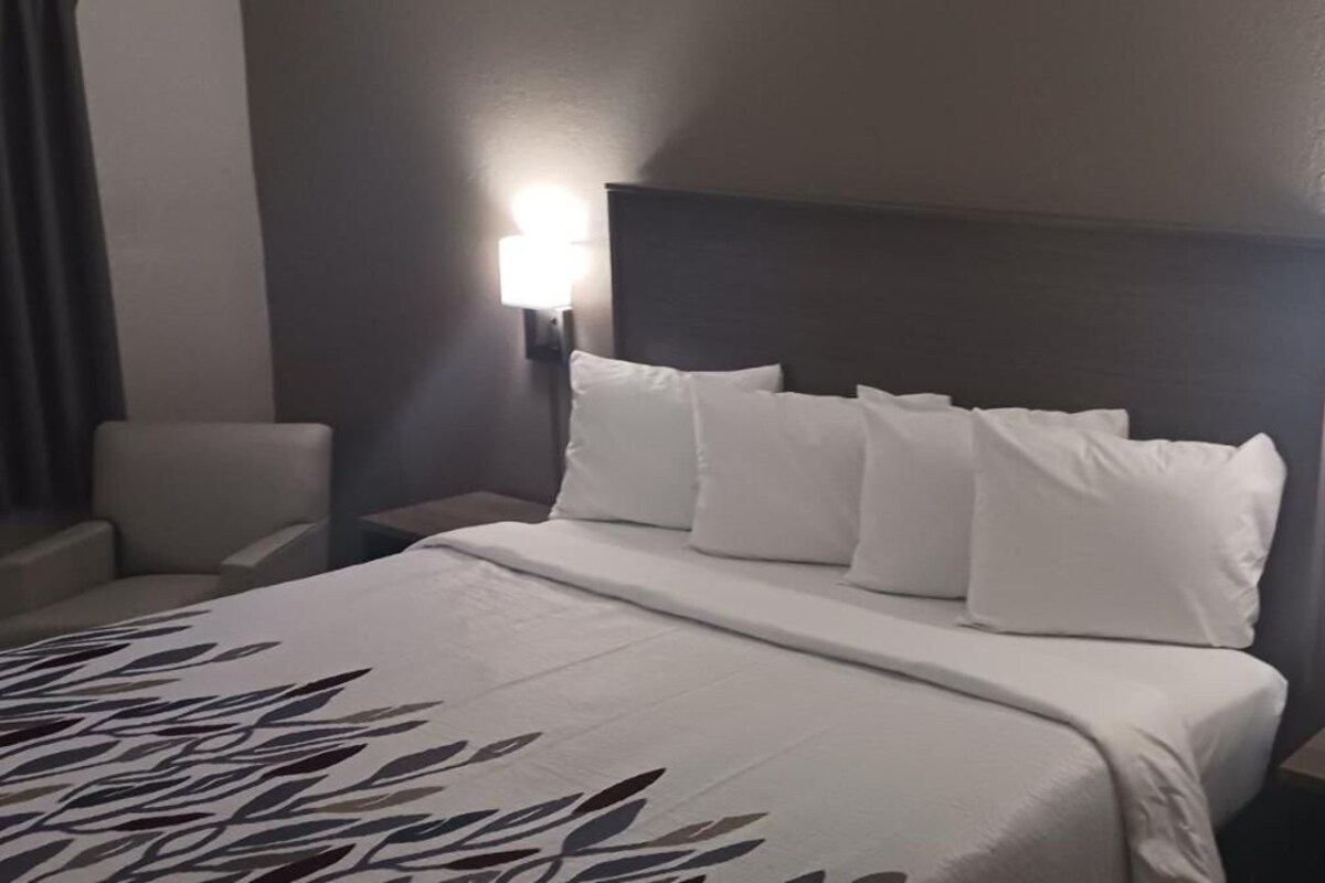 A hotel room with a bed, two bedside tables, a chair, and a wall-mounted lamp.