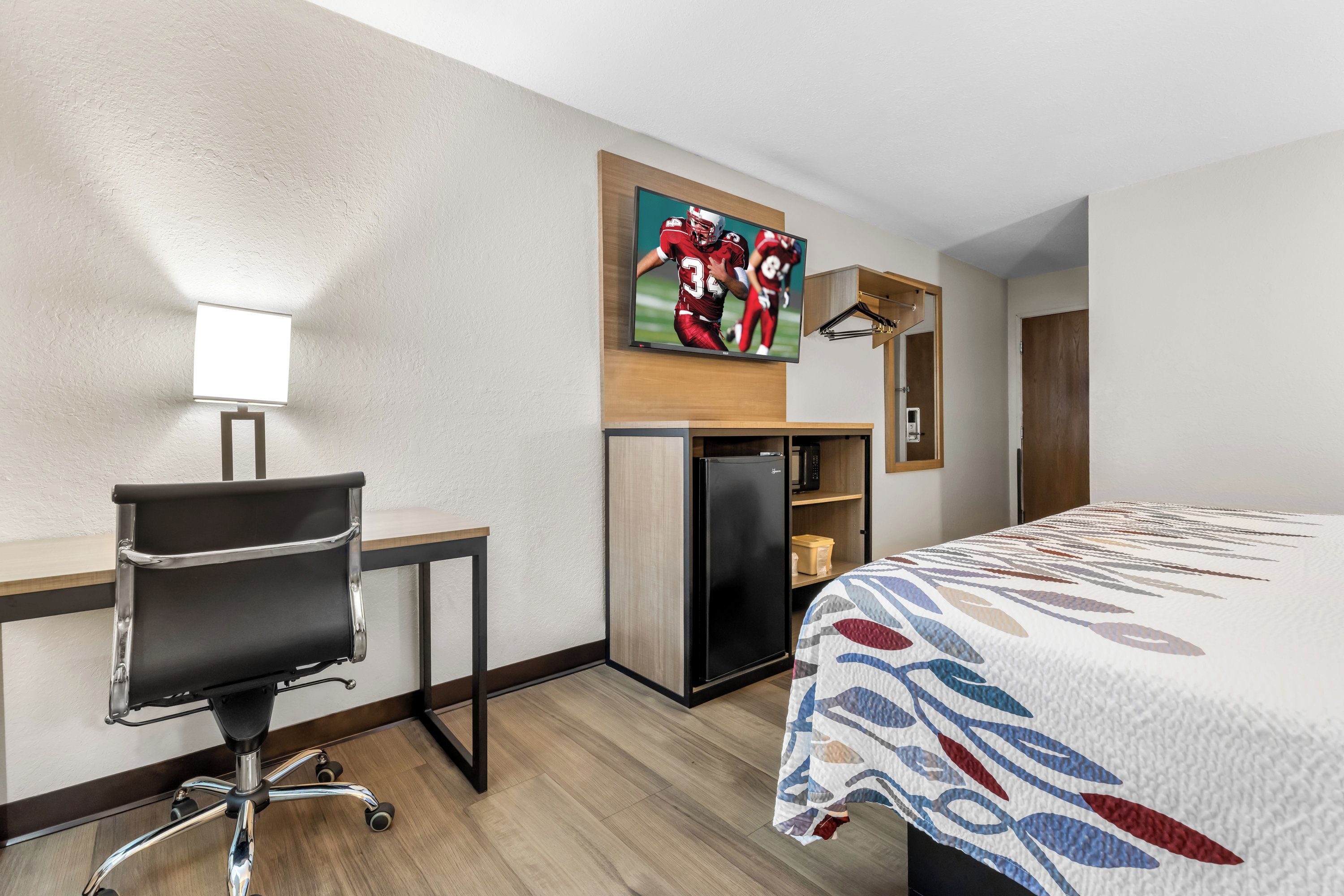 Une chambre d’hôtel comprenant un lit, un bureau avec une chaise, un téléviseur fixé au mur et un réfrigérateur.