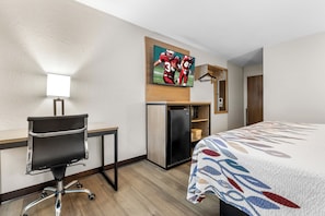 A hotel room with a bed, a desk with a chair, a television mounted on the wall, and a refrigerator. - Red Roof Inn Huntsville, AL (Huntsville)