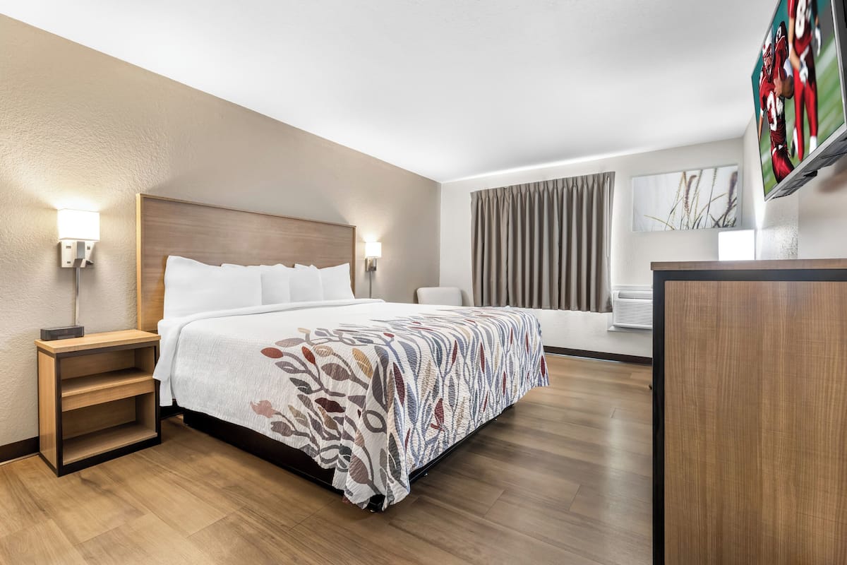 A hotel room with a large bed, a desk, a flat-screen TV, and a window with curtains.