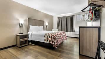 Une chambre d’hôtel comprenant un lit, des tables de chevet, une armoire, un miroir et une fenêtre avec des rideaux.