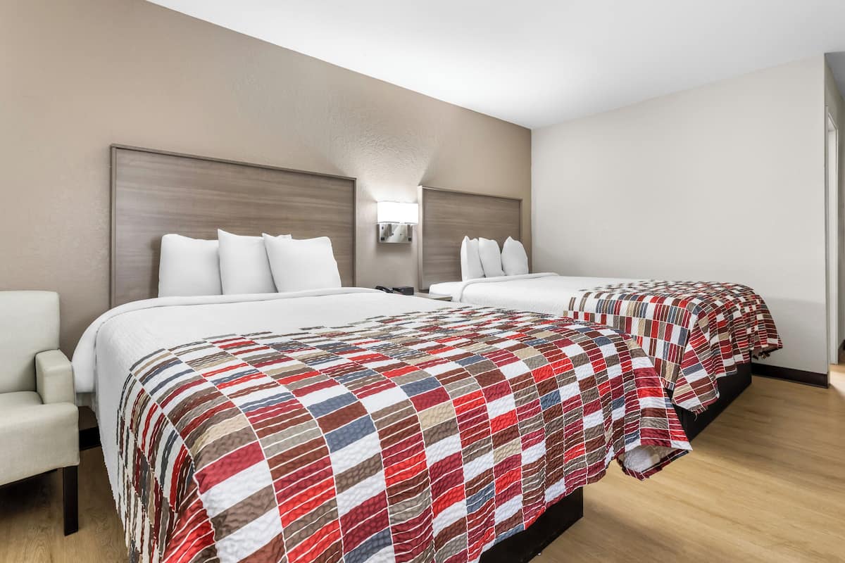 A hotel room with two beds, a nightstand, and a chair.