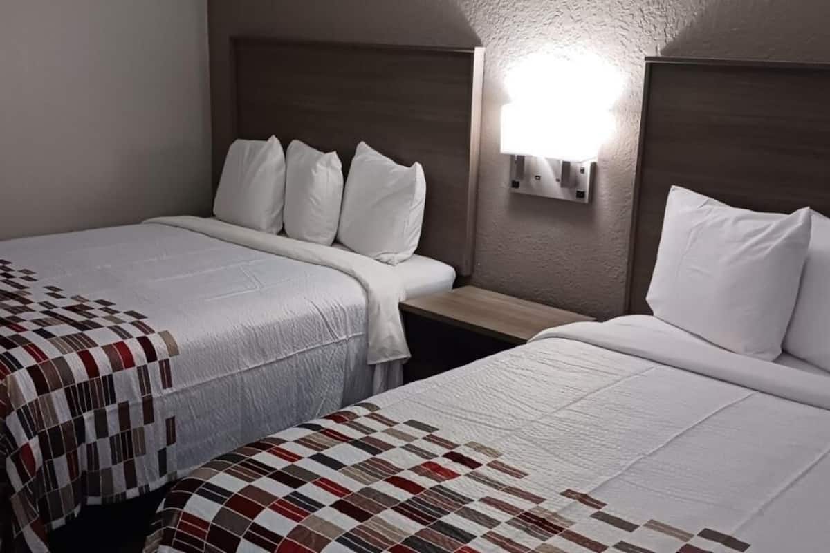 A hotel room with two beds, each with a quilted bedspread, a wooden headboard, and a wall-mounted light fixture.