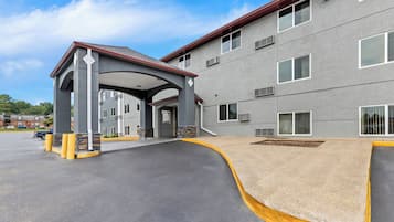A multi-story building with a covered entrance, a parking lot, and a landscaped area.