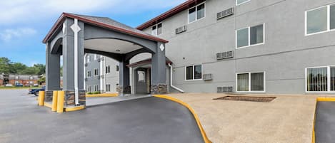 A multi-story building with a covered entrance, a parking lot, and a landscaped area.