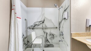A shower stall with a marble wall, a white chair, and a handrail.
