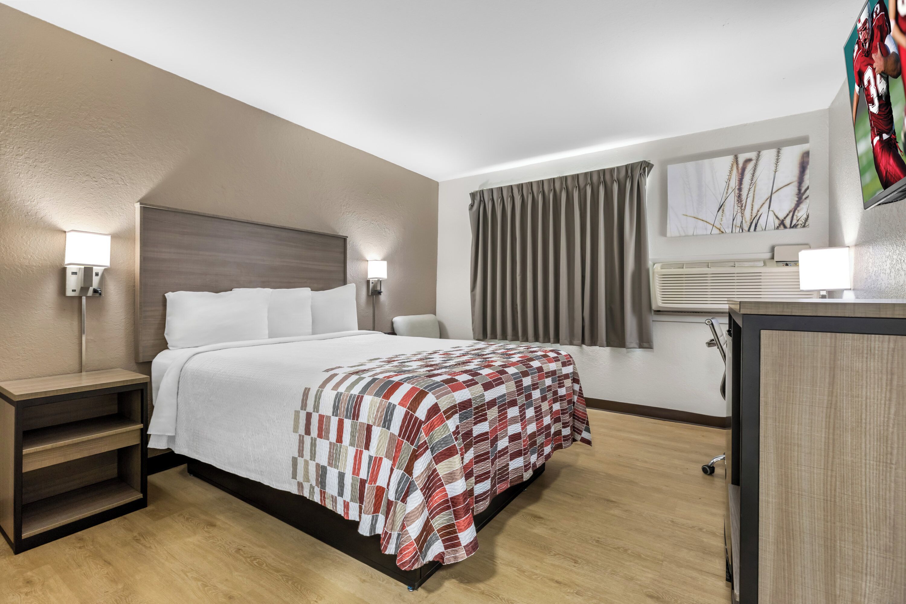 A hotel room with a bed, bedside tables, a desk, a TV, and a window with curtains.